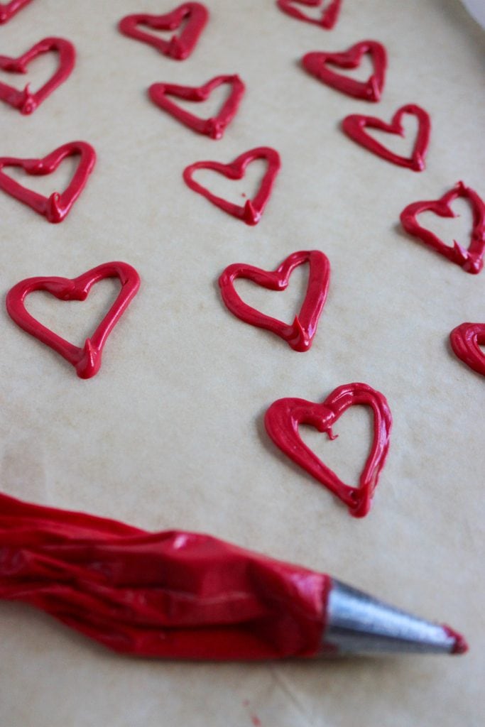 Chocolate hearts on parchment paper next to piping bag