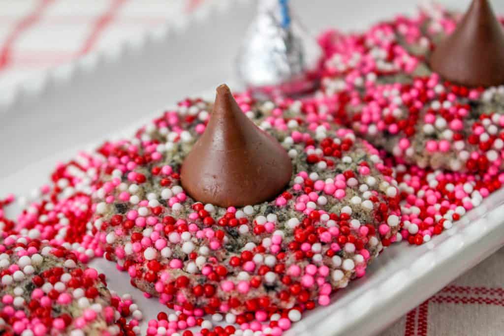 close up of blossom cookie with hershey's kiss in the center, on a plate of red and pink sprinkles