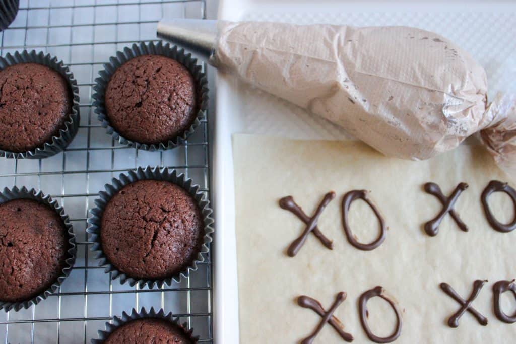 chocolate cupcakes next to piping bag of frosting and finished chocolate decorations