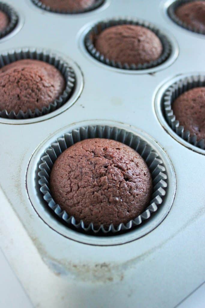 fully baked chocolate cupcakes in a cupcake tin with liners