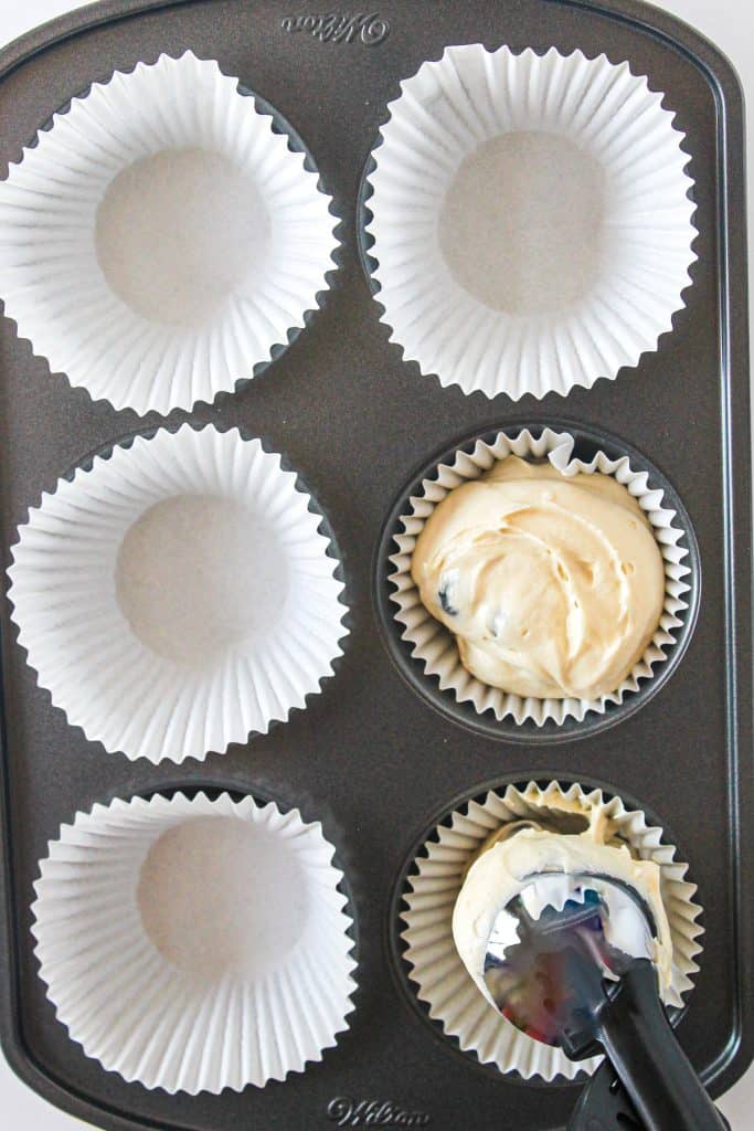 using a scoop to put muffin batter into jumbo muffin tin