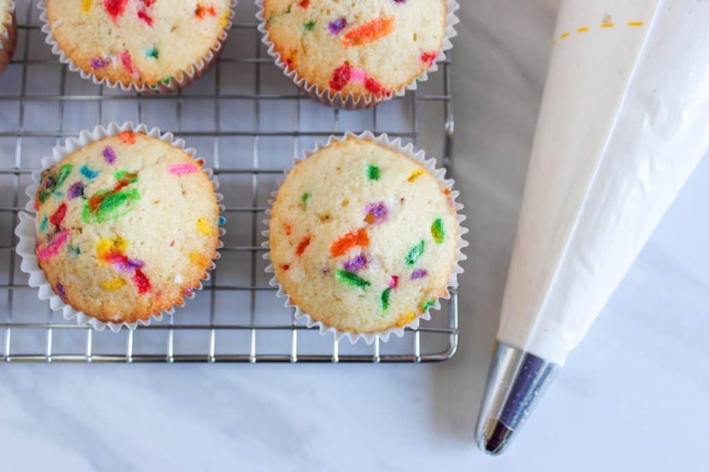 baked cupcakes on cooling rack next to piping bag of icing