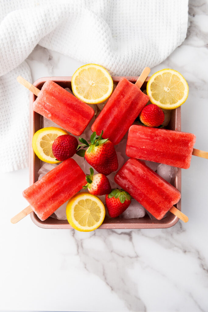 overhead shot of popsicles, strawberries, and lemons on a tray