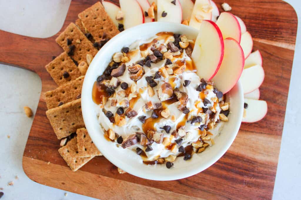 overhead shot of caramel Twix apple dip with apple slices and graham crackers on a cutting board