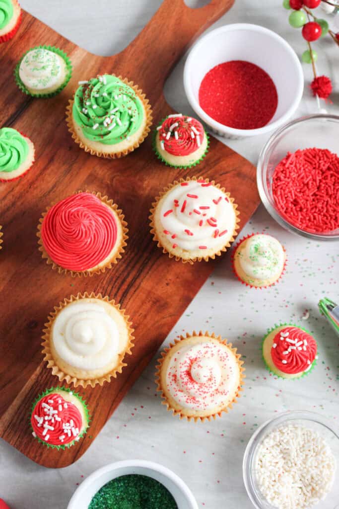 decorated cupcakes on board next to bowls of sprinkles and sugar