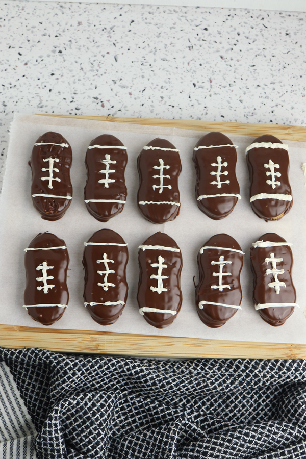 pipe the melted white candy onto the chocolate dipped cookies in the shape of football laces and allow to harden.