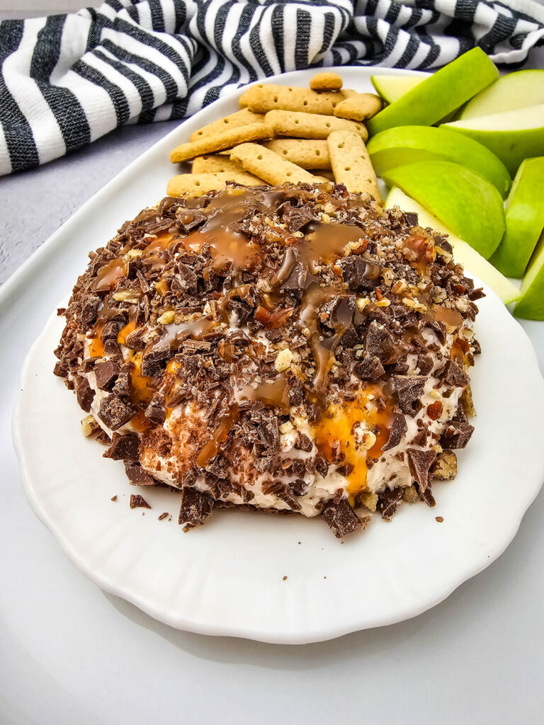 closeup of finished caramel apple cheesecake dip on a plate with fruit and cookies
