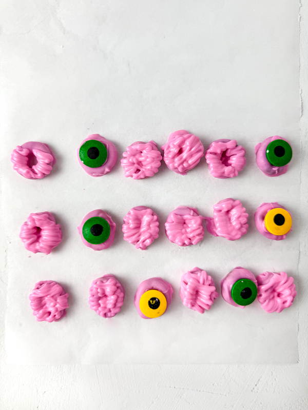 add candy eyes to half of the pink pretzels and create "brains" with the melted candy on the other half
