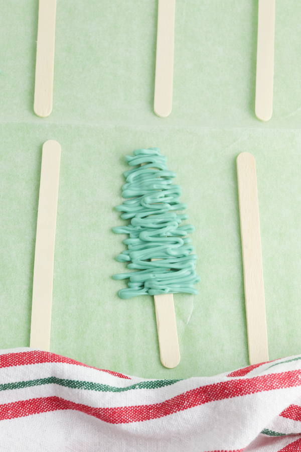 drizzle green candy in a triangle shapes across the popsicle sticks