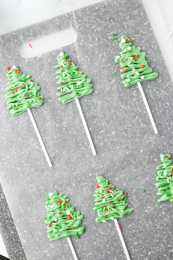 drizzle melted green candy over the popsicle sticks in a triangle shape. decorate with sprinkles.